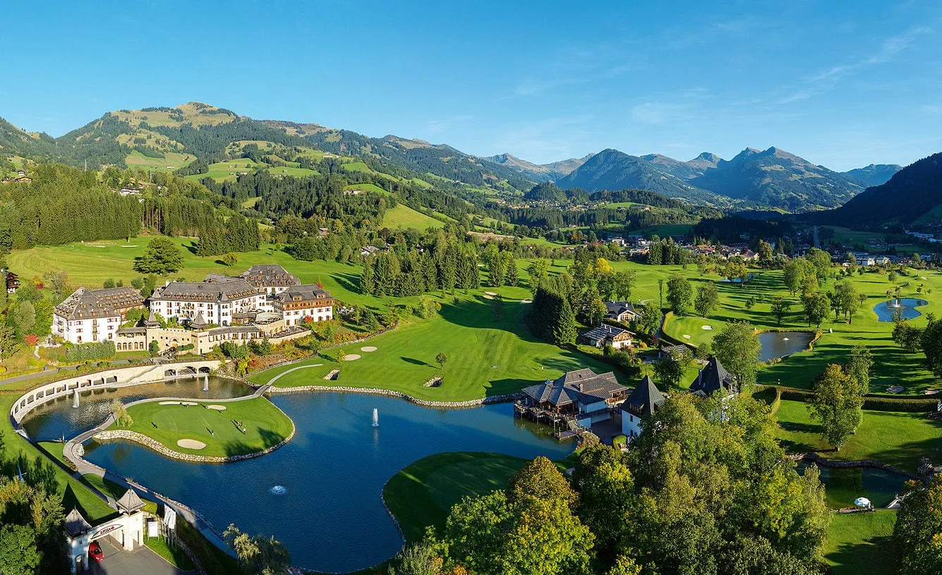 Schlosshotel Kitzbühel von oben, umgeben vom Golfplatz mit Teichen und Bergen