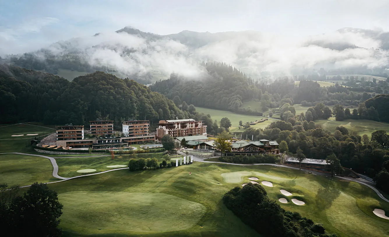 Grand Tirolia Kitzbühel über dem Golfplatz Eichenheim, dahinter Wolken über den Bergen